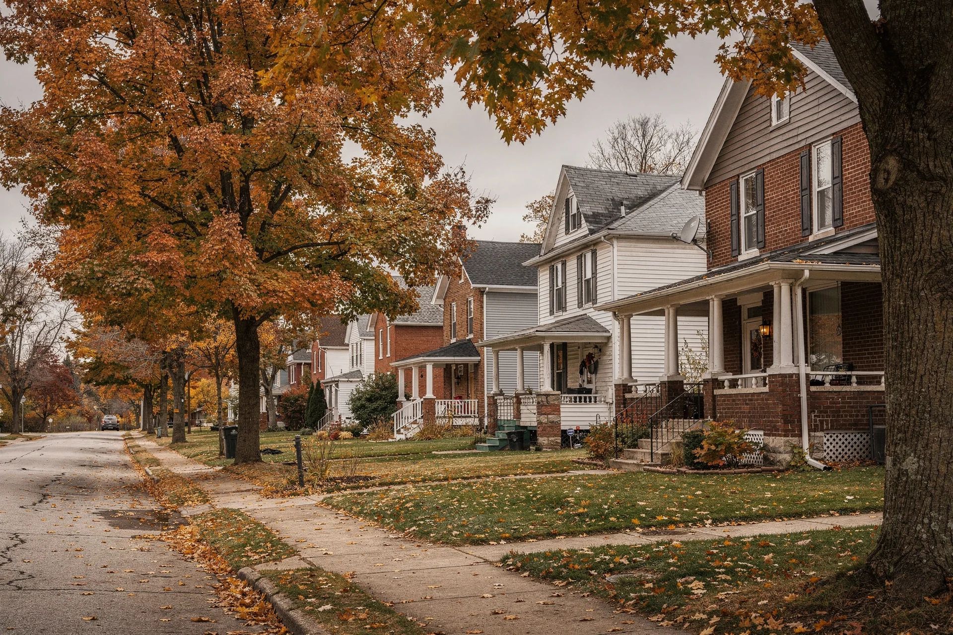 Older two-story homes with front porches along a tree-lined residential street in autumn